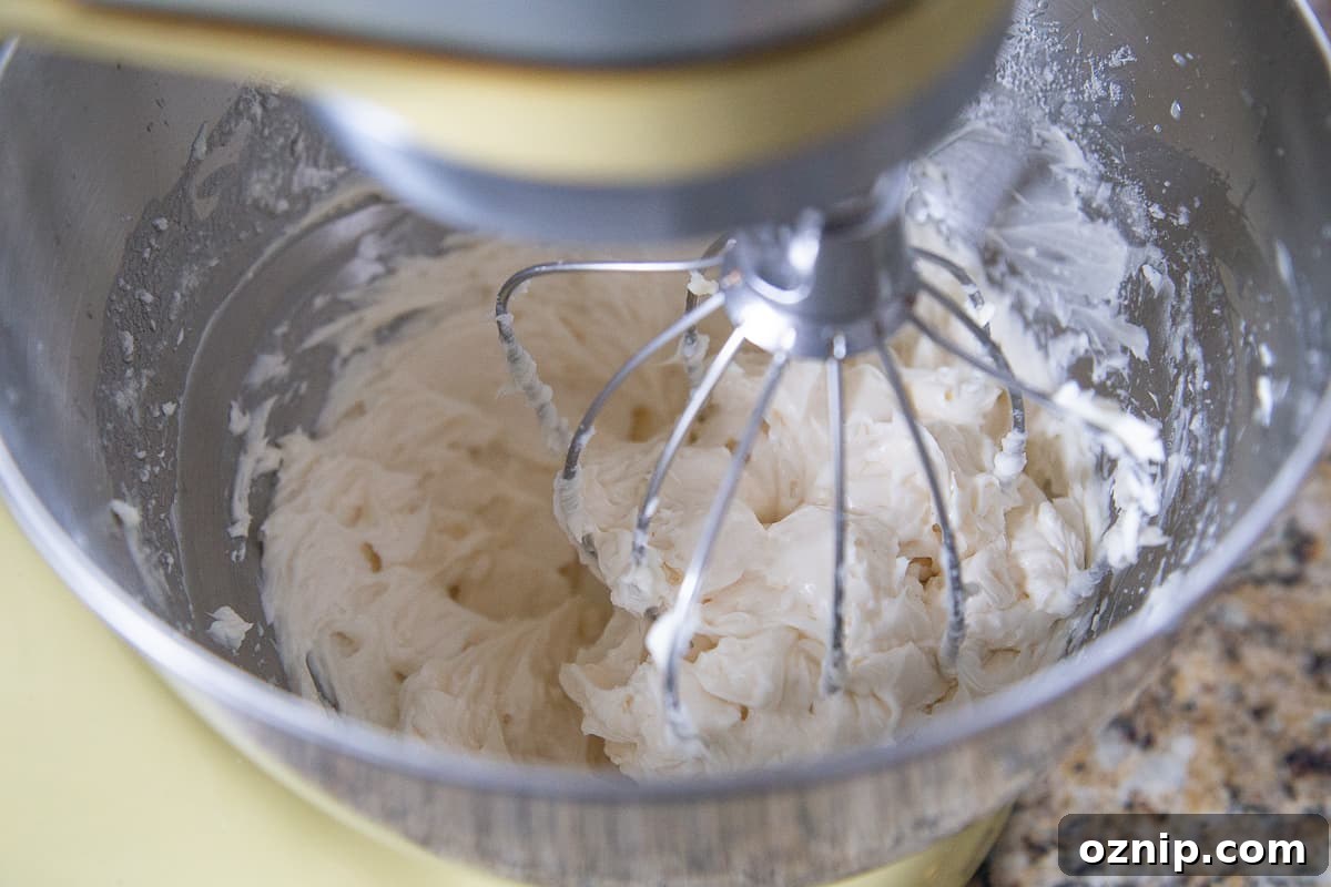 Stand mixer with a whisk attachment beating a creamy butter and sugar mixture.