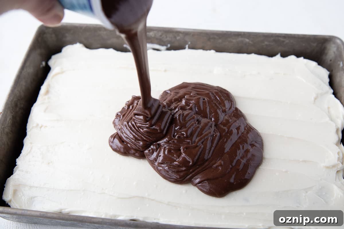 Hand pouring a can of chocolate frosting over a cake in a metal pan.