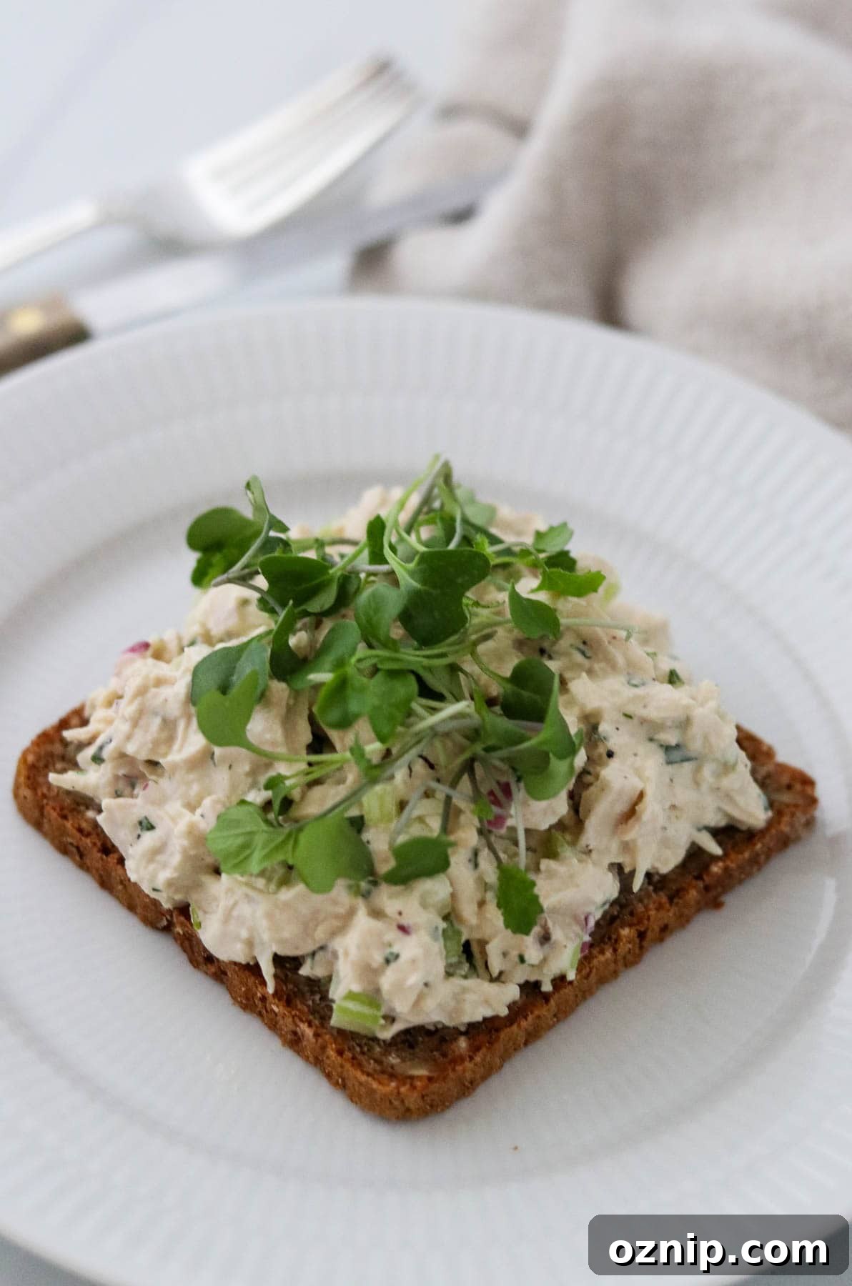 Chicken salad smørrebrød on a white plate next to a knife and fork.