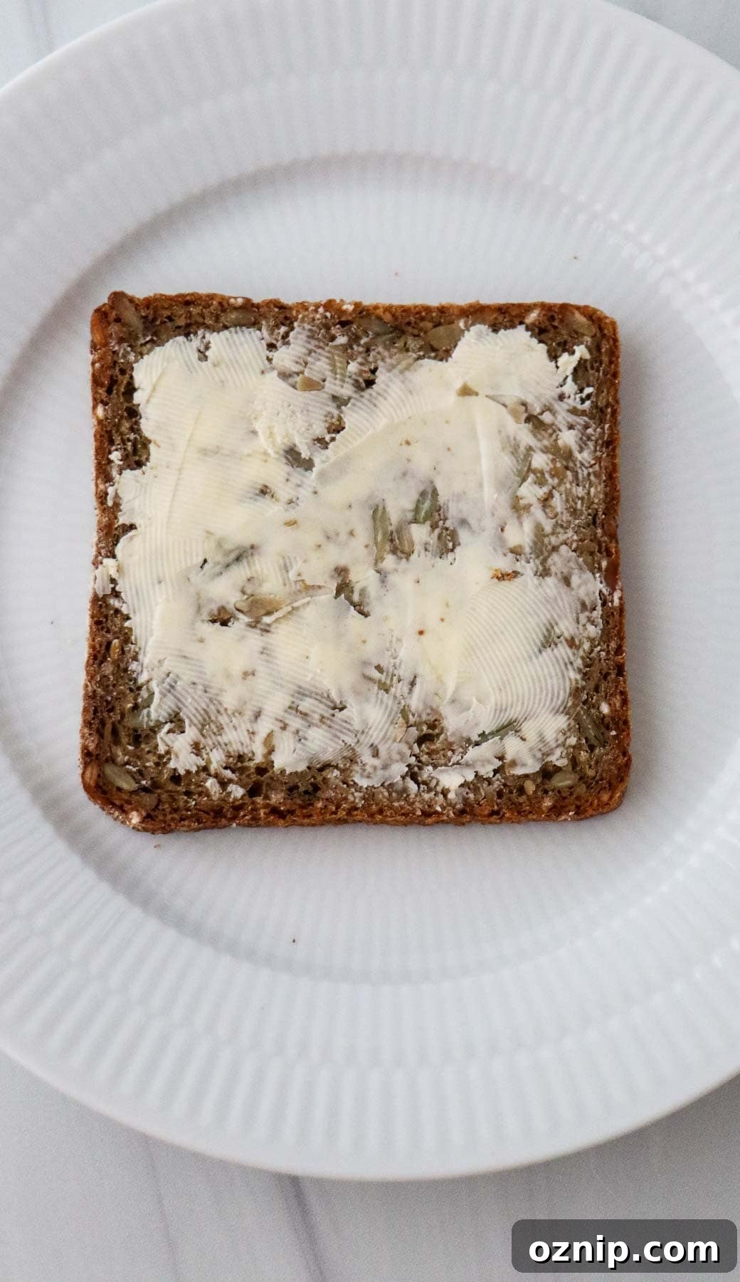 Slice of buttered rye bread on a white plate.