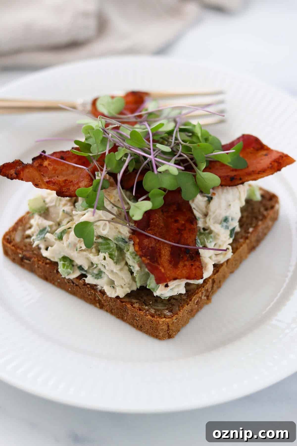 Chicken salad smørrebrød topped with bacon and microgreens.